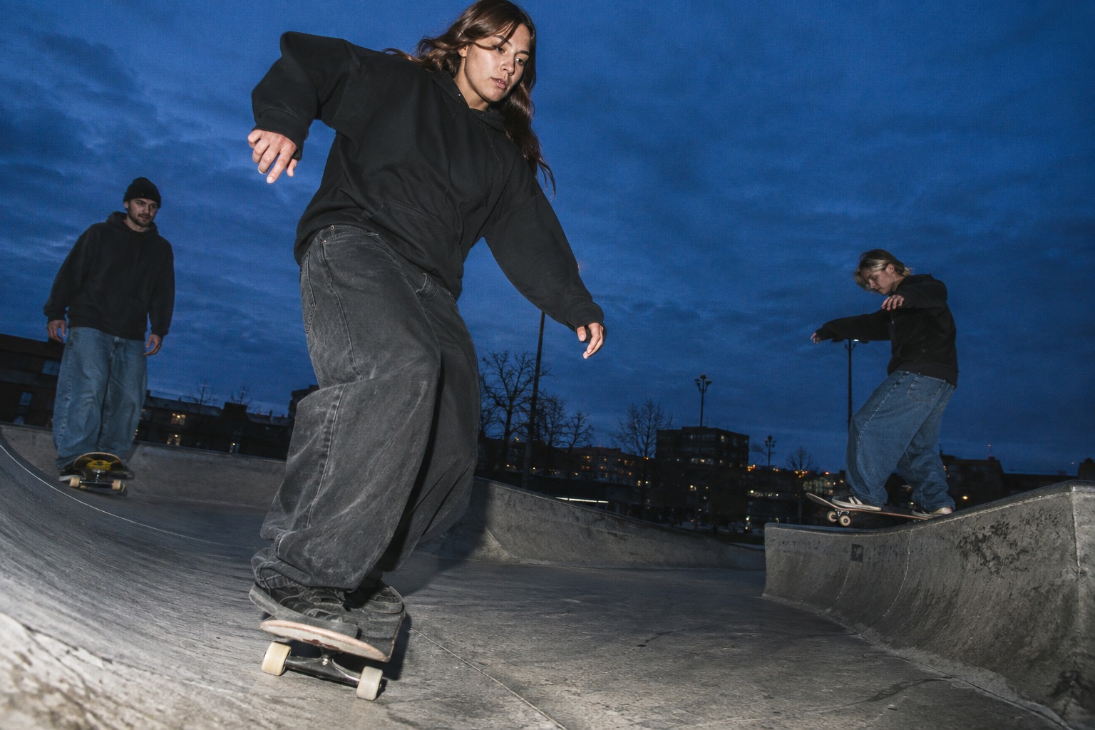 Skatere i løst streetwear på en betonbane i aftenlys